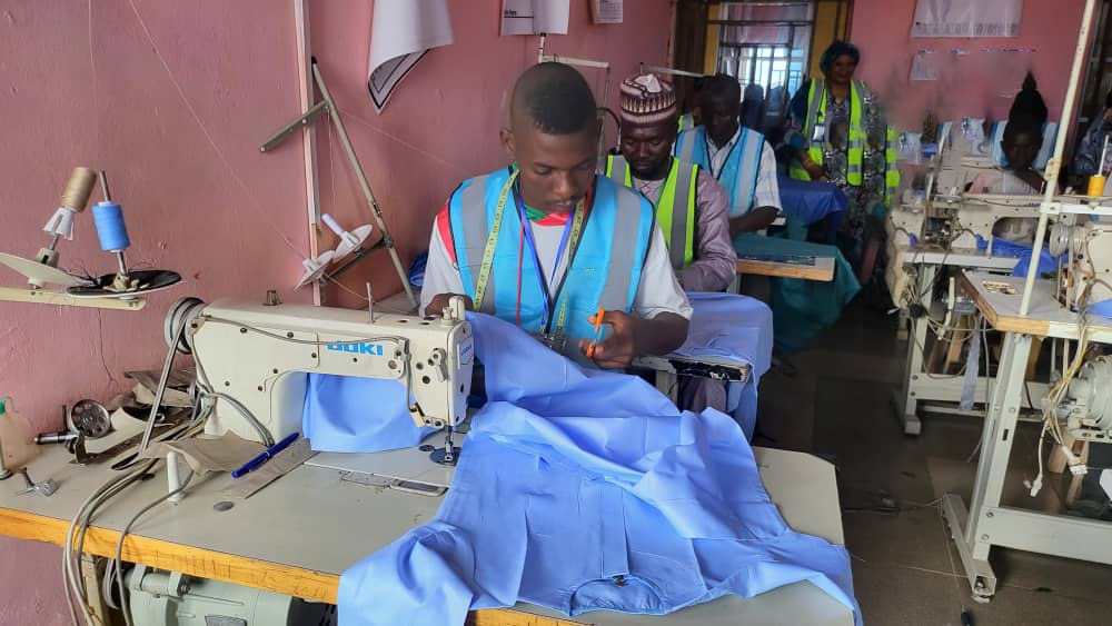 Male trainee at sewing machine with supervisor in background