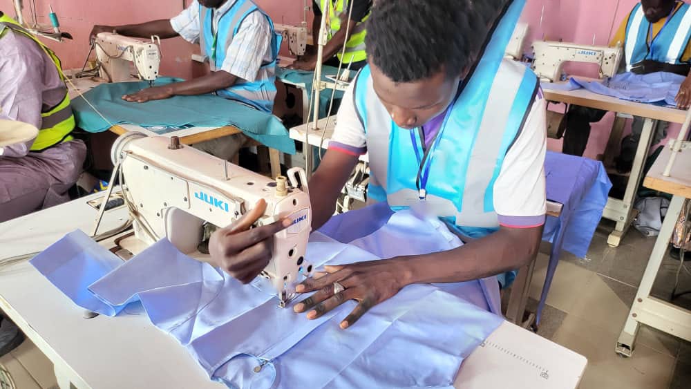 Trainee focused on sewing with peers at machines in the workshop