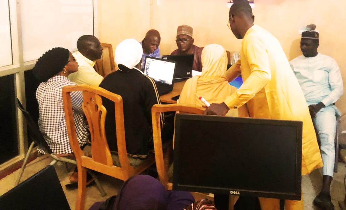 Group of participants gathered around laptops with facilitator standing