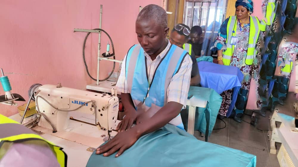Trainee at sewing machine being supervised by instructor in high-vis vest